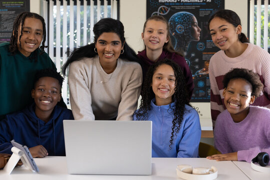 Diverse female students with mentor guiding around silver laptop at lab table showing AI poster