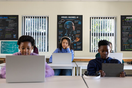 African American youth students sitting using silver laptops, dark tablet and headphones at school