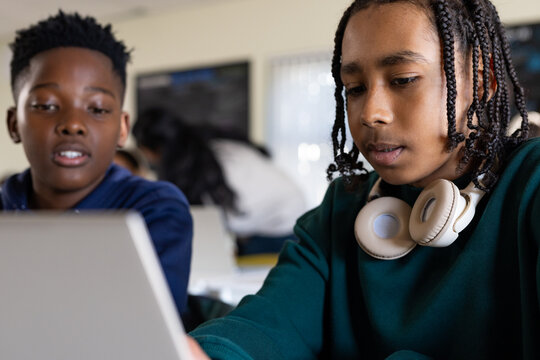 African American teenage boys collaborating on laptop at school desk wearing hoodies and headphones