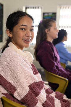 Three female teens sitting in classroom smiling with braces, striped sweater and headphones