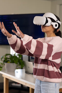 African American teenage woman wearing striped knit at desk reaching white VR headset, copy space