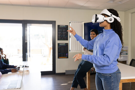 Teen classmates watching student wearing white VR headset gesturing in lab with laptop, copy space