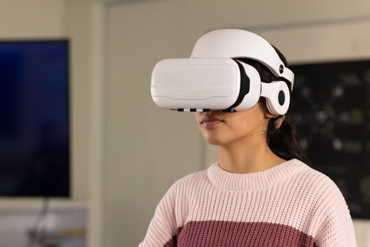 African American teenage female wearing white VR headset and exploring virtual lab with monitor