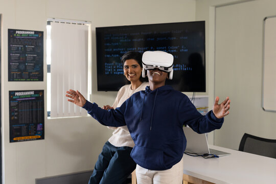 Male learner wearing white VR headset reaching in tech lab, female trainer observing code monitor
