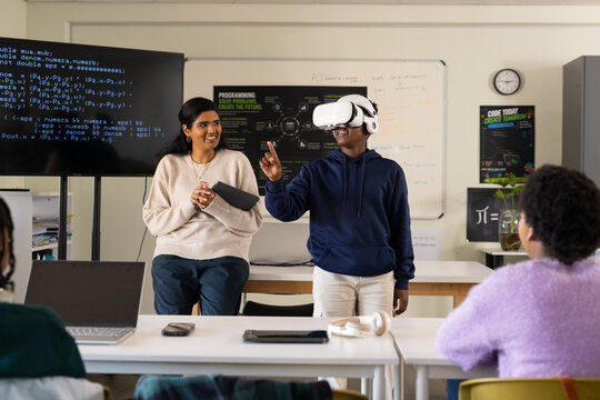 Diverse class watching African American teenager using VR headset while Indian teacher using laptop