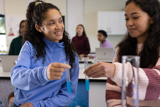 Two teenage female students holding test tubes with blue liquid in school science lab, smiling