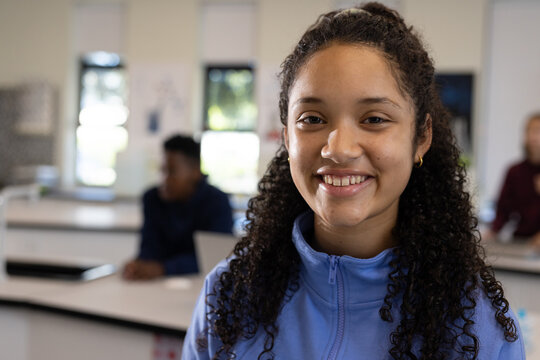 African American teenage student smiling at camera in class wearing light blue jacket with laptop
