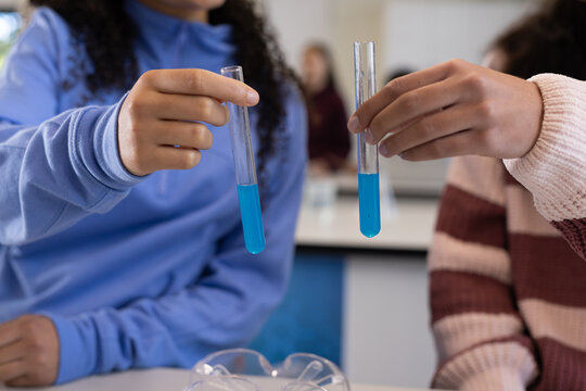 African American teen females holding blue test tubes at school lab with goggles on bench, sweaters
