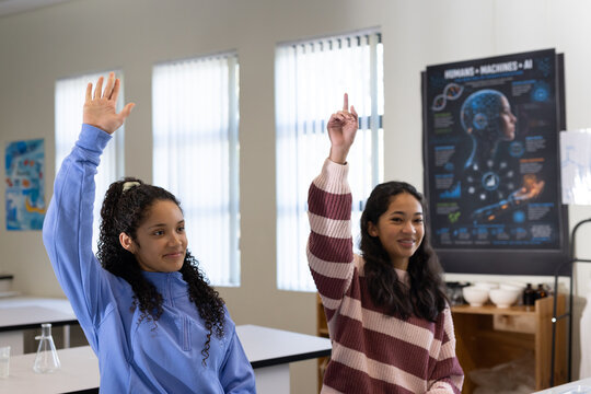 African American teenage girls sitting at lab tables in science class raising hands with flask
