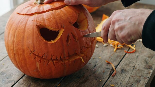 A close up view of a person carving a spooky face into a fresh orange pumpkin for the halloween holiday