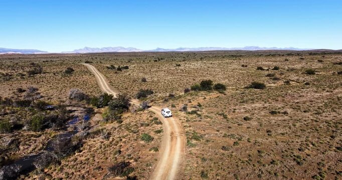 Aerial drone photograph of a white 4x4 vehicle travelling along a winding gravel road beside a seasonal river in the Great Karoo near Prince Albert, Western Cape, South Africa.