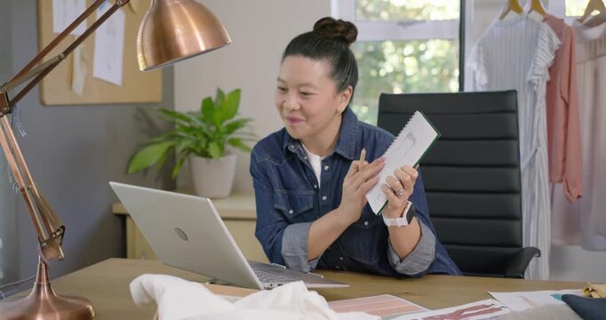 Asian woman showing notebook, flipping pages and comparing fabric swatches with laptop for feedback