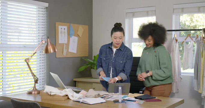 Diverse female team sorting swatches using tablet showing yellow sample picking fabric in studio