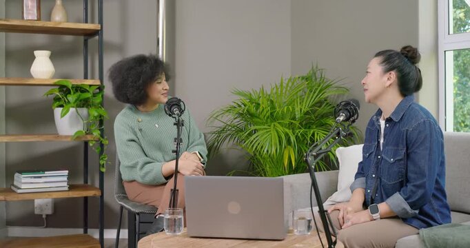 Diverse female cohosts shaking hands, discussing while recording podcast with mics at studio table