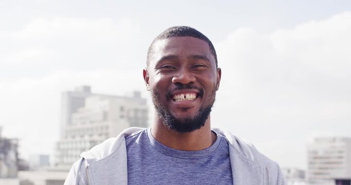 Mid-adult African man standing on rooftop facing camera in hoodie and T-shirt, smiling and laughing