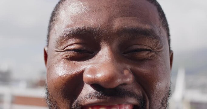 Mid adult African American man smiling, revealing tooth gap while camera starting close-up rooftop