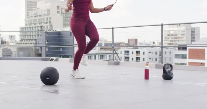 Woman lifting knee, rotating jump rope, skipping for cardio on roof, maroon set, fitness tracker