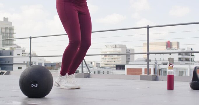 Woman starting skipping rope, maroon leggings on rooftop for cardio, med ball left, bottle right