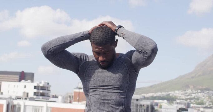 Mid-adult man stretching and recovering on rooftop after run, breathing and wearing compression top