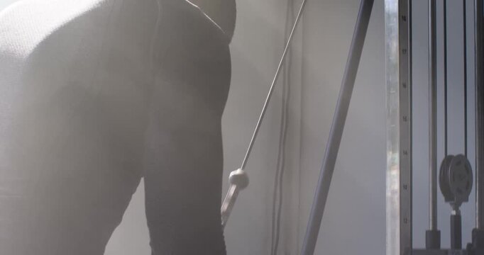 African man gripping double-rope carabiner, pulling cable down for strength reps by window