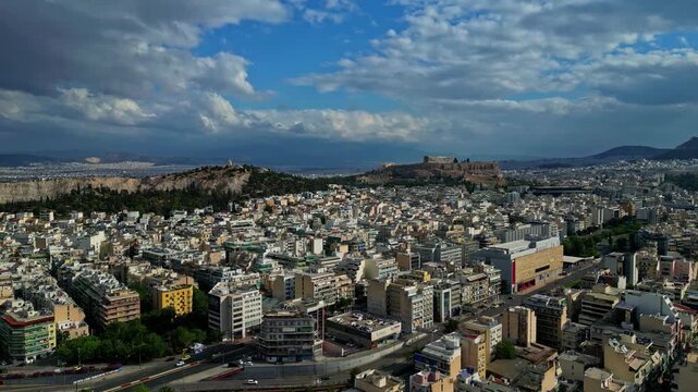Aerial view of the historic Acropolis of Athens overlooking the dense urban cityscape under a blue sky with scattered clouds in Athens, Greece.