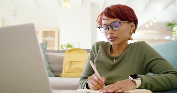 African American woman in olive top and glasses responding to laptop while writing and typing notes