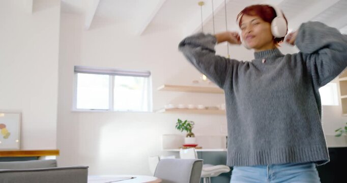 African American woman putting on white headphones, adjusting fit, dancing to music in kitchen
