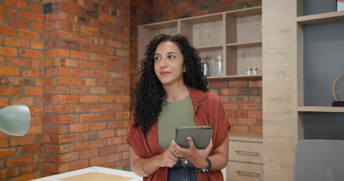 African American woman holding tablet, tapping after notification, reviewing notes for work at desk