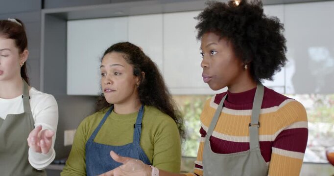 Three women in aprons discussing steps shaping dough on kitchen island placing pieces in muffin tin