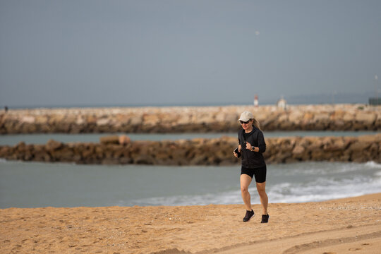 Sporty blonde woman running ocean beach. Young caucasian female exercising outdoors running seashore. Concept of healthy running and outdoors exercise. Active, sporty athlete jogging. Summer active