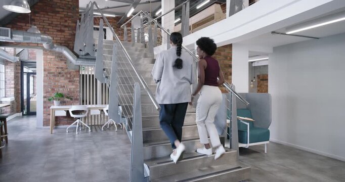 Diverse female coworkers after brief talk climbing metal stairs at office for meeting with tablet