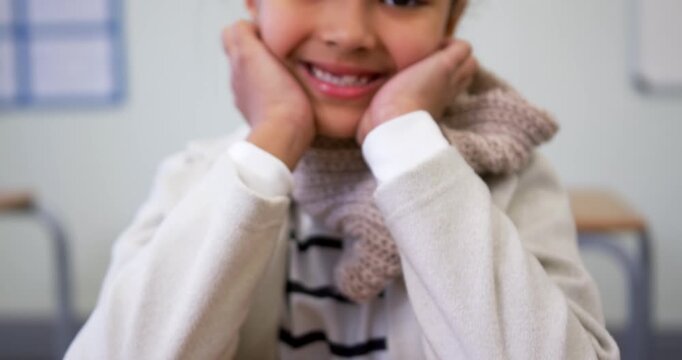 School-age girl resting arms on desk in class, camera panning up, posing and smiling with scarf