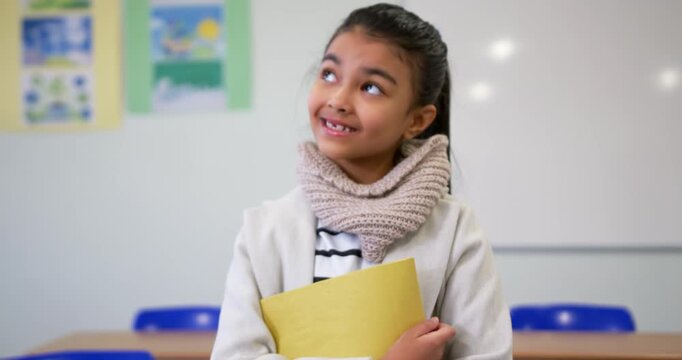 Camera pulling back causing schoolgirl holding yellow folder and scarf looking up, smiling in class