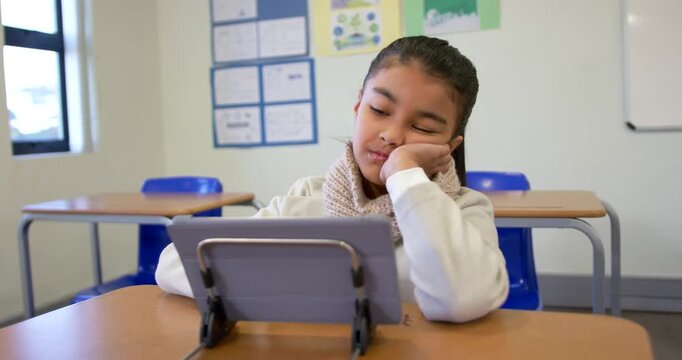 African American child pupil sitting at school desk propping head gazing at tablet on stand waiting