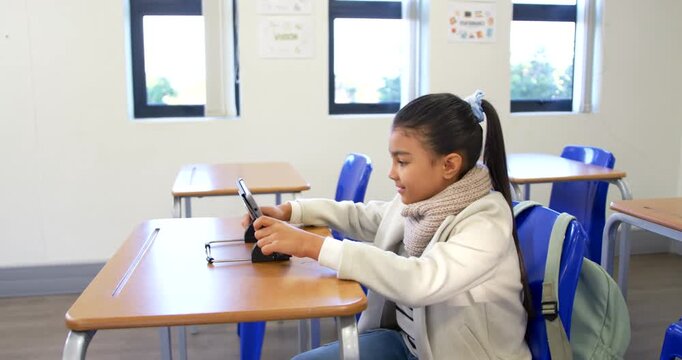 African American child sitting at desk in class, adjusting tablet on stand, tapping, backpack