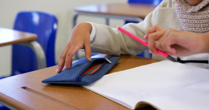 African American teen girl reaching blue pencil case, selecting pink pencil, drawing at school desk