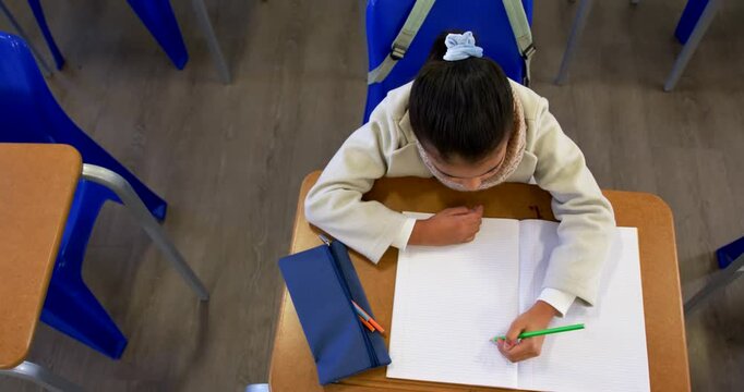 African-American teenage student writing in notebook with green pencil in classroom, taking notes