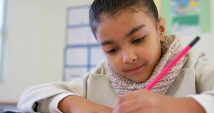 African American child starting classwork at school, writing with pink pencil wearing scarf smiling