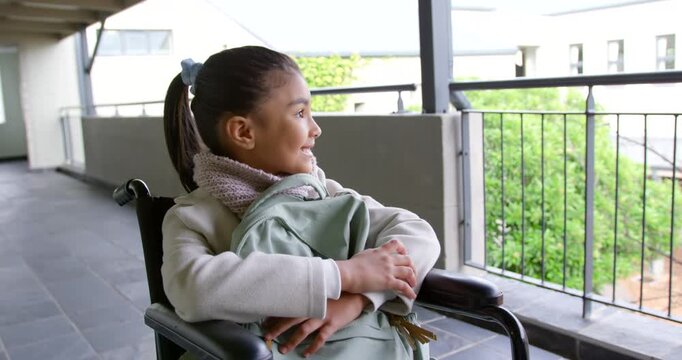 African American preteen sitting in wheelchair holding backpack, seeing camera, smiling on balcony