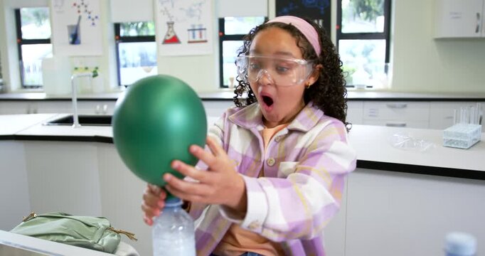 Preteen African American with goggles placing balloon on bottle at school lab, watching gas rising