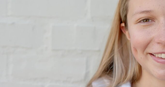 Teenage female after camera shift turning to camera, smiling with dimples at brick wall, copy space