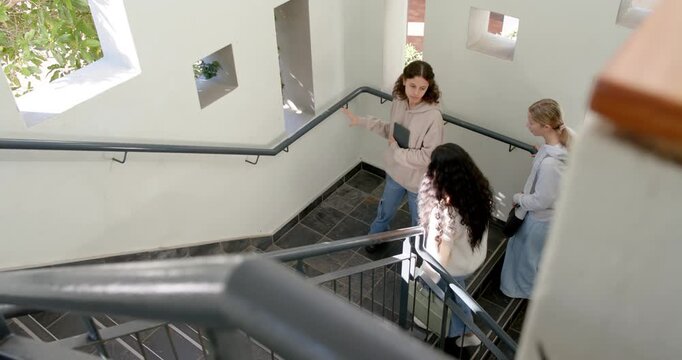 Diverse females reaching stair landing, leader pausing, gesturing, holding tablet and sharing notes