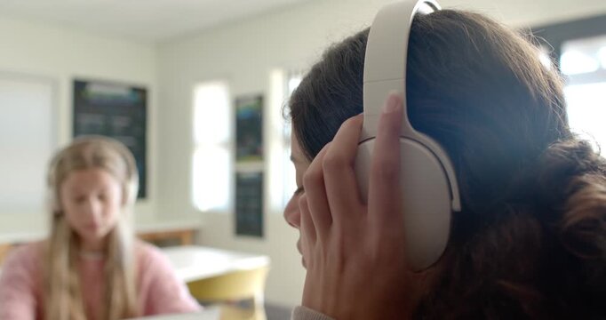 Two teen girls getting over-ear headphones placed by hand in classroom, adjusting fit studying