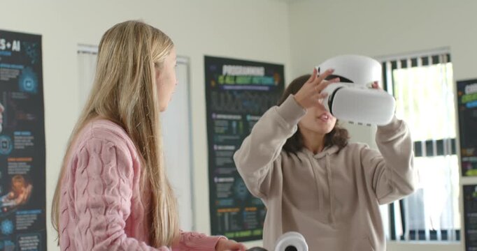 Two teen girls right girl beige-hoodie placing VR headset left holding controller testing for class