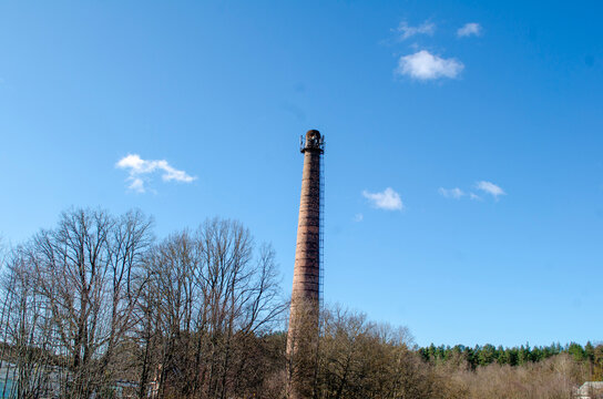 Old brick chimney stands tall against blue sky at a forested area in the afternoon
