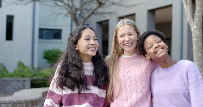 Camera cuing teen girl friends in sweaters posing for picture laughing leaning in courtyard by wall