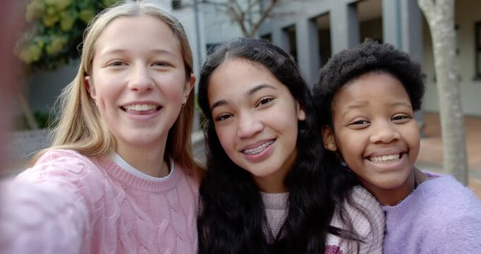 Diverse teenage female friends left girl holding phone taking selfie hugging braces on campus