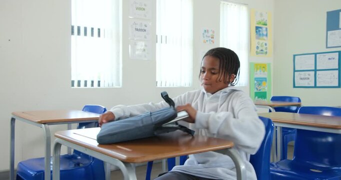 African American teen male entering class, placing bag, opening silver laptop, preparing to work