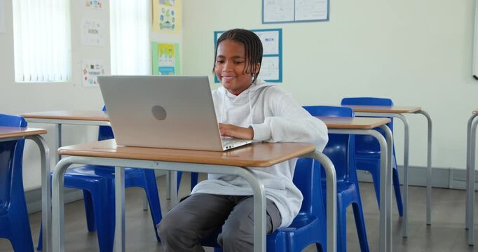 African male youth student sitting at desk in class typing on laptop glancing rubbing head studying