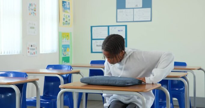Teen African male in gray hoodie finding empty school desk placing backpack opening laptop to study